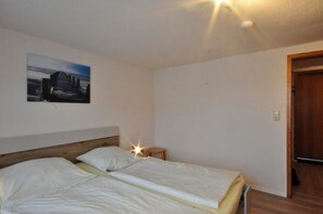 A room with a bed, a small table, a wall-mounted light, and a door. - Vacation Apartment, Bahnhofstraße 8, Apt. 1 (Wittmund)