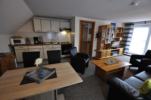 Un espace de vie compact comprenant un coin cuisine, un espace repas avec une table et des chaises, un canapé et un téléviseur dans le salon.
