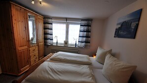 Une chambre avec deux lits, une armoire en bois, une fenêtre avec des rideaux à rayures et un tableau accroché au mur.