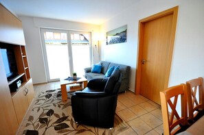 Una sala de estar con un sofá, una mesa de centro, un televisor y una puerta.