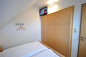 A bedroom with a bed, a wooden wardrobe, a TV mounted on the wall, and a coat hanger.