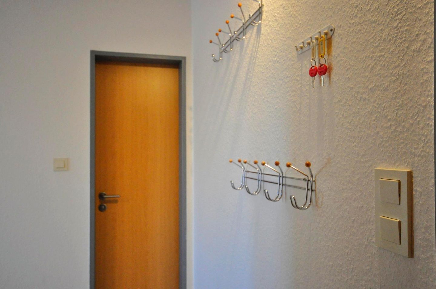 Ein Flur mit einer Holztür, einem an der Wand befestigten Kofferständer mit Haken und einem Lichtschalter.