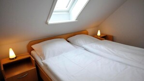 En enkeltseng med hvide sengetøj, to sengeborde og et ovenlysvindue.