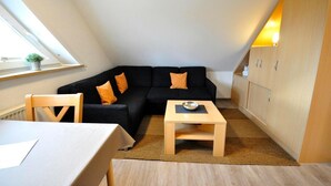 Et lille, hyggeligt værelse med en sort sofa, et træbord og et skab.