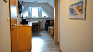 En smal gang fører til et spiseområde med et bord og stole, et lille tekøkken og et vindue med udsigt over det fri.