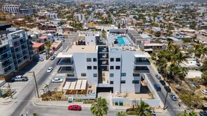 A modern multi-story building with a central courtyard, surrounded by residential areas and palm trees. - Beautiful New Condo Centrally Located in Cabo! (Cabo San Lucas)
