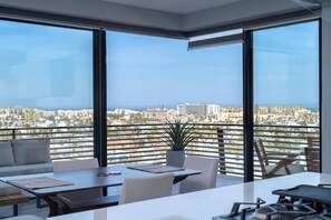 A modern dining area with a city view, large windows, and a balcony with a plant. - Beautiful New Condo Centrally Located in Cabo! (Cabo San Lucas)