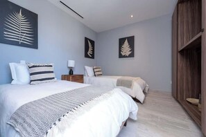 A bedroom with two beds, a nightstand, a lamp, and artwork on the walls. - Beautiful New Condo Centrally Located in Cabo! (Cabo San Lucas)