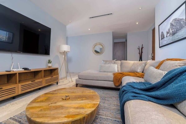A modern living room with a large flat-screen TV, a round coffee table, a sofa, and a sideboard. - Beautiful New Condo Centrally Located in Cabo! (Cabo San Lucas)