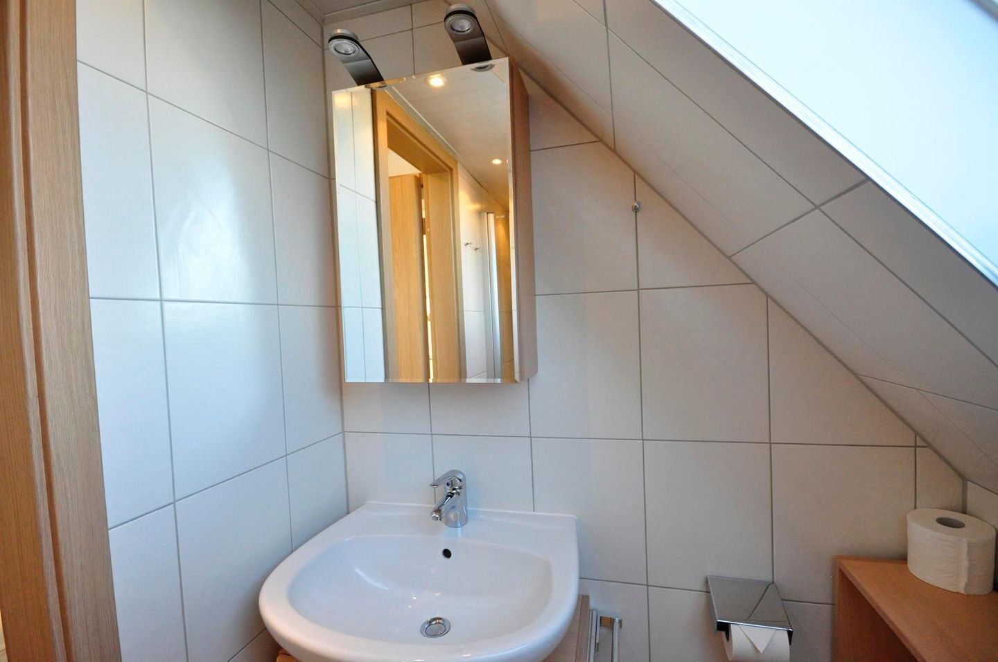 Ein Badezimmer mit weißem Waschbecken, einem Spiegel und einer Toilette.