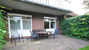 A patio with a table and chairs, a brick wall, and a hedge.