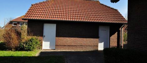 A two-story brick building with a red-tiled roof, two white doors, and a small garden area with grass and shrubs.