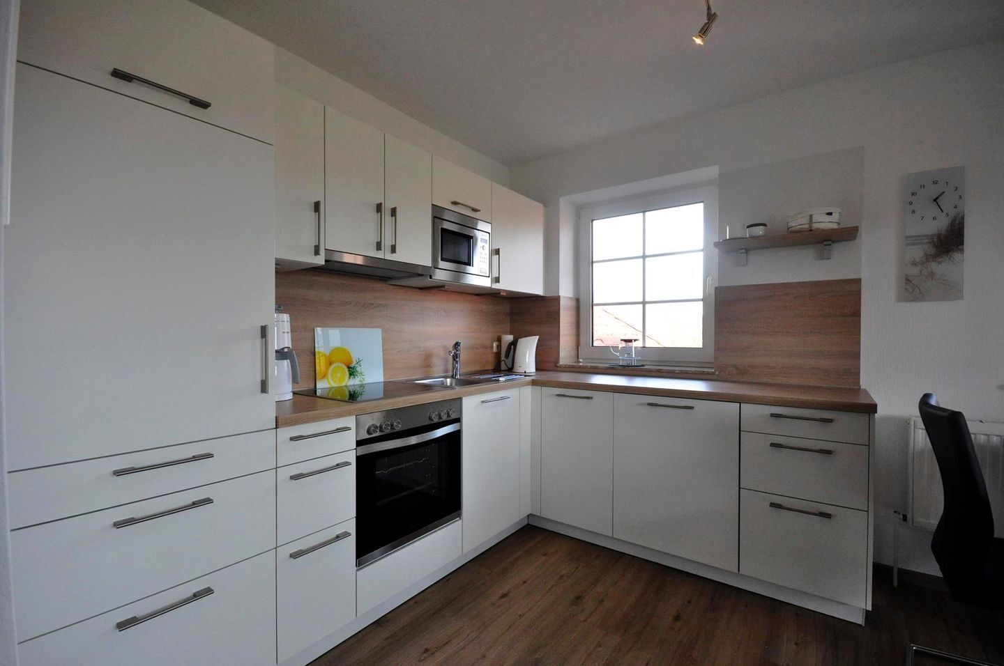 Een moderne keuken met witte kastjes, een magnetron, een oven en een raam dat voor natuurlijk licht zorgt.