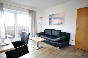 Un salon moderne avec un canapé en cuir noir, une table basse en bois et un coin repas comprenant une chaise et une table.