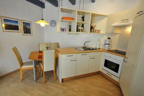 A compact kitchen with a wooden dining table, chairs, a built-in oven, and a sink.