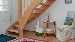 Un escalier en bois dans une pièce dont le mur est blanc, un petit arbre à chat en bois, une chaise blanche avec un coussin vert et un tapis rouge et blanc sur le sol.