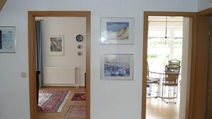 Un couloir doté d’un plancher en bois, d’un radiateur et d’une porte donnant sur un coin repas avec une table et des chaises.