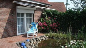 Une maison en briques avec un patio couvert, un petit étang orné de nénuphars et une chaise.
