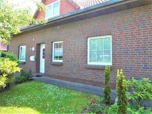 Ein zweistöckiges Ziegelhaus mit einer Haustür, zwei Fenstern und einem kleinen Vorgarten mit Gras und Blumen.