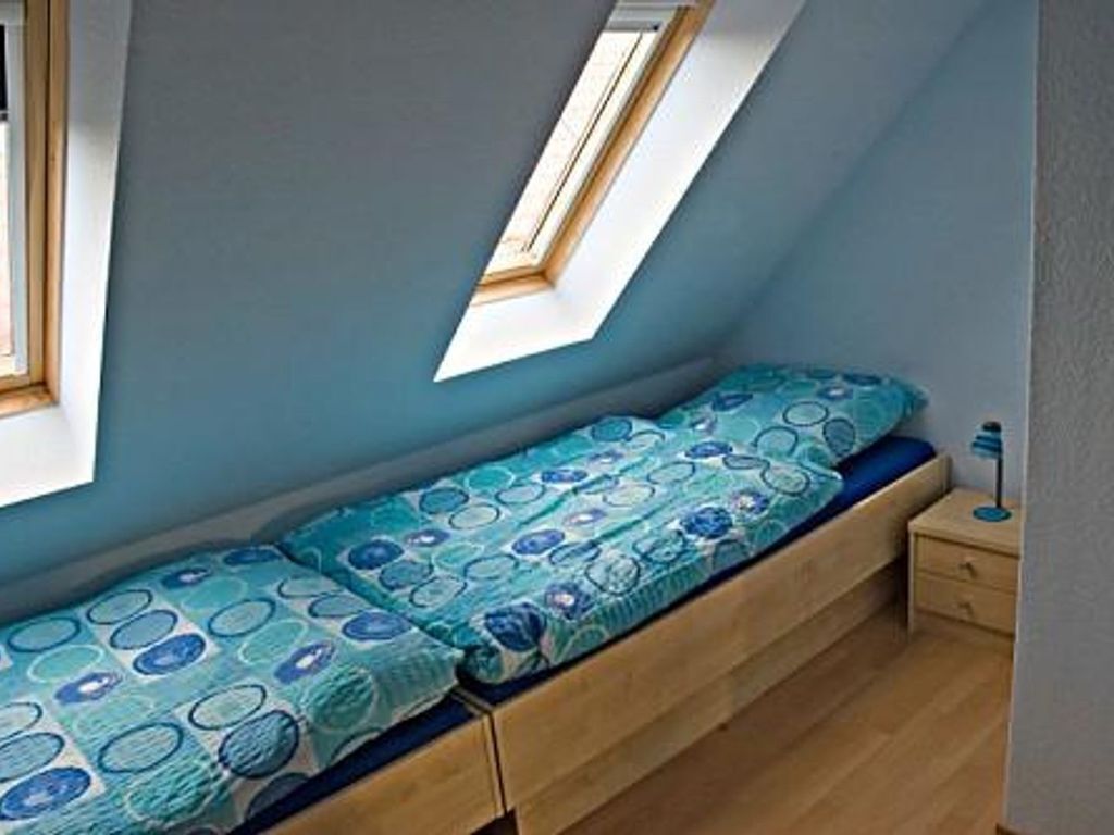 A small, single-bed room with a sloped ceiling and skylight, wooden flooring, and a bedside table with a lamp.