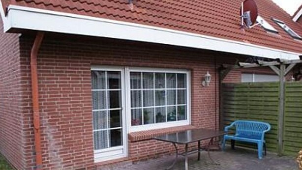 A brick house with a tiled roof, a large window, a metal table, and a blue chair in the backyard.