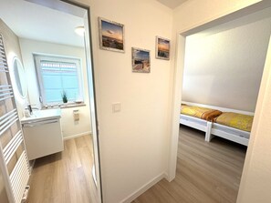 Ein Schlafzimmer mit Bett, Fenster mit Jalousien, einem kleinen Nachttisch und einem an der Wand hängenden Bild.