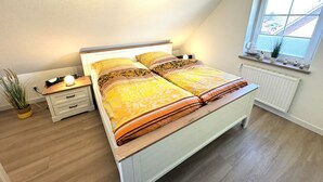 Un dormitorio con cama, mesitas de noche, ventana y radiador.