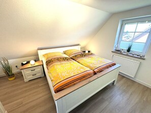 Un dormitorio con cama, mesitas de noche, ventana y radiador.