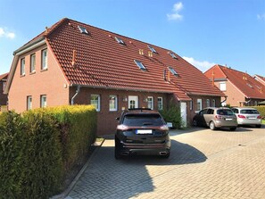 Ein Wohngebäude mit rotem Ziegeldach, einer gepflasterten Auffahrt und einem schwarzen Auto im Vordergrund.