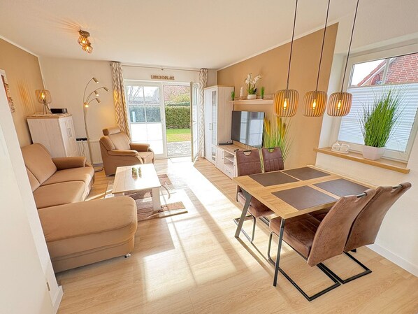 Una sala de estar moderna con un sofá, una mesa de comedor con sillas, un televisor y una zona de cocina.