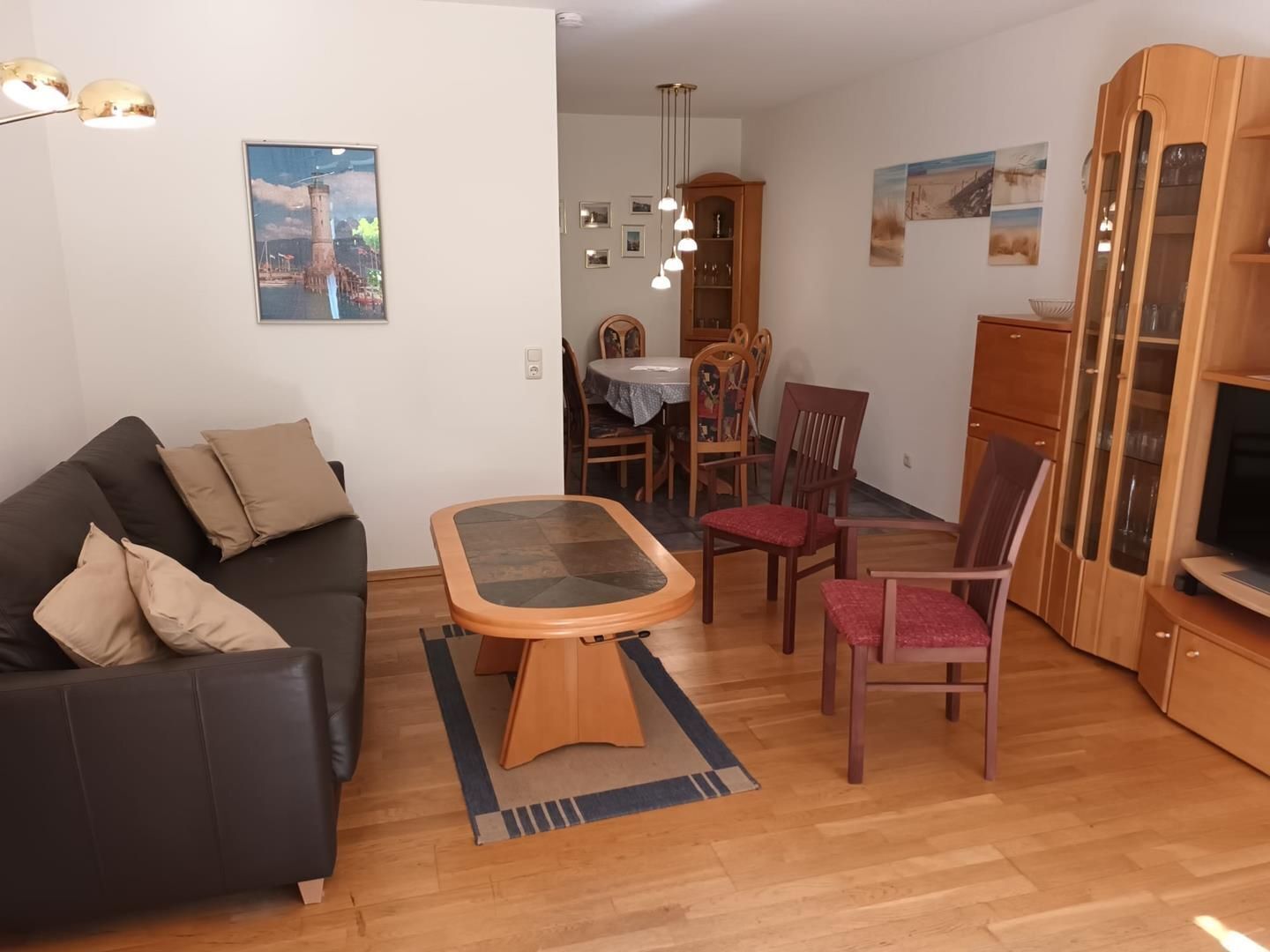 A living room with a black sofa, a wooden coffee table, a dining table with chairs, and a TV cabinet.