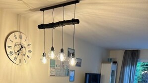 Een eetgedeelte met een houten tafel en witte stoelen, een klok aan de muur en een televisie op de achtergrond.