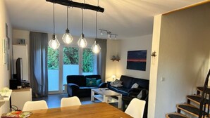 Een moderne woonkamer met een houten eettafel, witte stoelen, een zwarte bank en een trap.