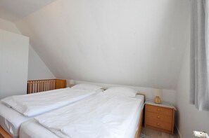 Ein Schlafzimmer mit zwei Betten, einem Holzkopfstück, einem Nachttisch mit Lampe und einem Fenster mit Vorhängen.