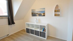 Una habitación con techo inclinado, una consola blanca con estantes, un cuadro de un paisaje y una pequeña repisa decorativa con un barco modelo.