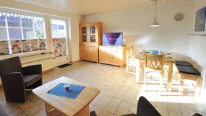 A spacious living area with a wooden table, chairs, a TV, and a cabinet. - Vacation home Uferstraße 19b (Wittmund)
