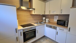 A modern kitchen with white cabinets, a built-in oven, a stovetop, a microwave, and a coffee maker. - Vacation home Uferstraße 19b (Wittmund)