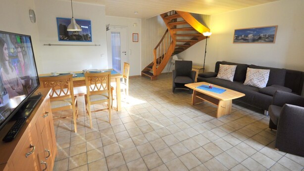 A living room with a wooden staircase, a TV, a dining table with chairs, a sofa, and a coffee table. - Vacation home Uferstraße 19b (Wittmund)