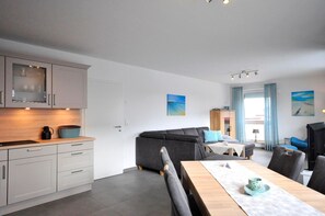 A modern kitchen with grey cabinets and a dining area with a wooden table and chairs. - Vacation w. Int Seeburger Winkel 5 OG - Holiday apartment Int Seeburger Winkel 5 OG (Wittmund)