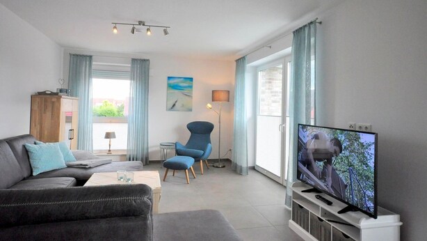 Un salon moderne avec un canapé, un fauteuil, une télévision et une vue sur l’extérieur.