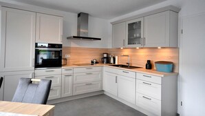 Une cuisine moderne avec des armoires blanches, un four noir, une hotte en acier inoxydable et un plan de travail en bois.