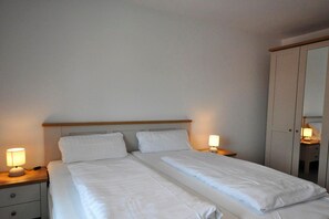 Cama doble con dos mesitas de noche, cada una con una lámpara, en una habitación con armario y espejo.