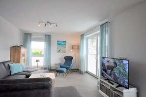 A modern living room with a sofa, armchair, TV, and a view of the outdoors. - Vacation w. Int Seeburger Winkel 5 OG - Holiday apartment Int Seeburger Winkel 5 OG (Wittmund)