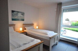 A hotel room with two single beds, a painting on the wall, and a view of the outside through a large window. - Vacation w. Int Seeburger Winkel 5 OG - Holiday apartment Int Seeburger Winkel 5 OG (Wittmund)