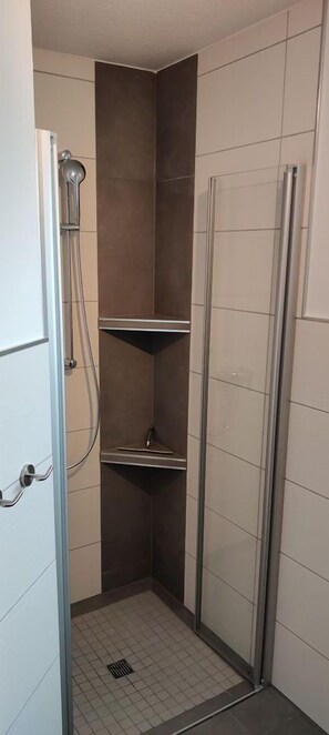 A small, enclosed shower area with a glass door, a metal showerhead, and a tiled floor. - Vacation w. Int Seeburger Winkel 5 OG - Holiday apartment Int Seeburger Winkel 5 OG (Wittmund)
