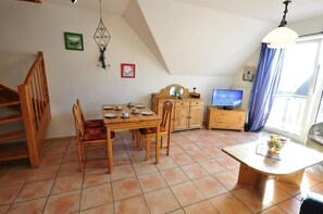 Ein Essbereich mit Holztisch und -stühlen, einem Fernseher und einem Fenster mit Vorhängen.