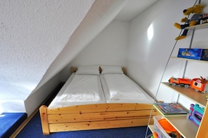 Ein kleiner, schräger Raum mit einem hölzernen Bett, weißer Bettwäsche und einem blauen Teppich.