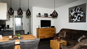 A modern living room with a wooden dining table, leather sofas, and a TV on a wooden cabinet. - Vacation home Krabbenpadd 9 "Find's Huus" - Holiday home "Find's Huus" Krabbenpadd 9 (Wittmund)