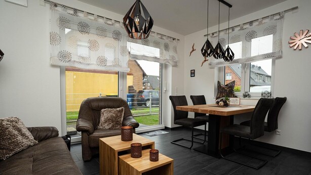 A modern living room with a sofa, a wooden coffee table, and a dining area with chairs and a table. - Vacation home Krabbenpadd 9 "Find's Huus" - Holiday home "Find's Huus" Krabbenpadd 9 (Wittmund)