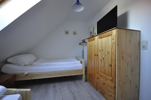 A small, single-bed room with a sloped ceiling, a wooden wardrobe, and a small table.